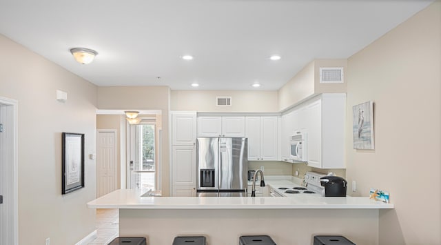 kitchen with a kitchen breakfast bar, white cabinetry, white appliances, and kitchen peninsula