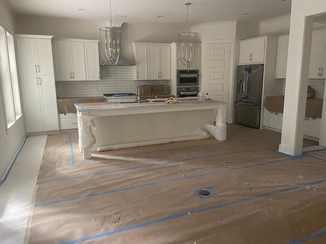 kitchen with wall chimney exhaust hood, stainless steel appliances, a kitchen island with sink, and white cabinets