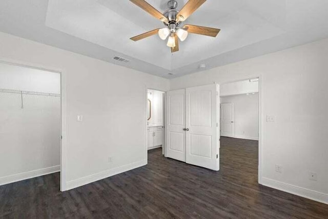 unfurnished bedroom featuring a closet, a tray ceiling, dark hardwood / wood-style floors, and a spacious closet