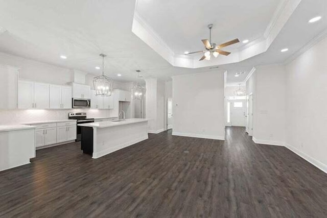 kitchen with crown molding, stainless steel appliances, a tray ceiling, an island with sink, and white cabinets