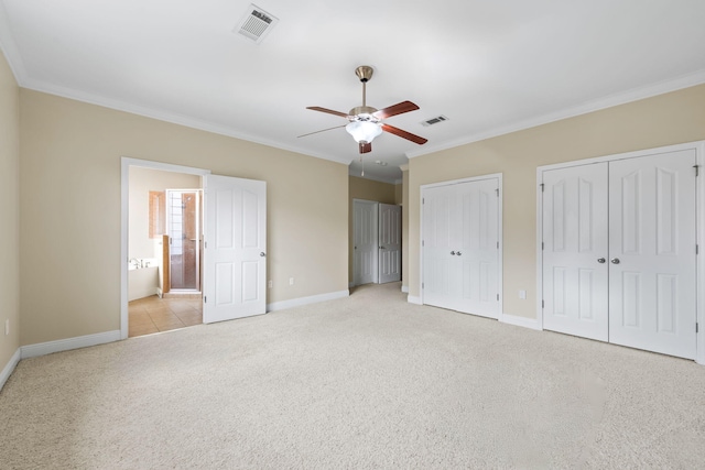 unfurnished bedroom featuring crown molding, ensuite bath, ceiling fan, light colored carpet, and multiple closets