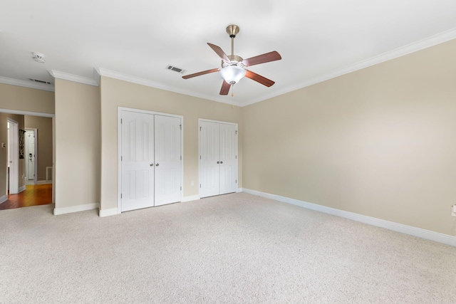 unfurnished bedroom with multiple closets, crown molding, carpet, and ceiling fan