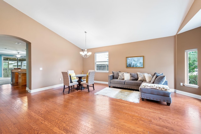 living room with wood-type flooring, a healthy amount of sunlight, ceiling fan with notable chandelier, and high vaulted ceiling