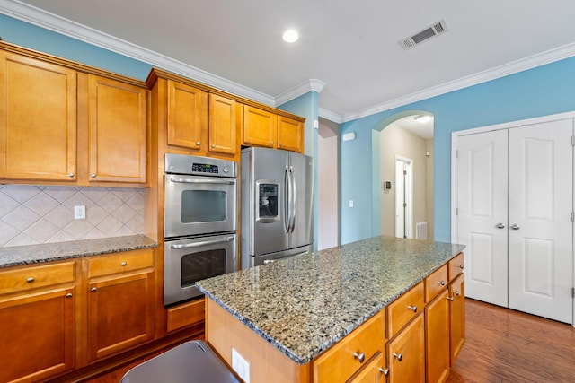 kitchen featuring appliances with stainless steel finishes, decorative backsplash, a center island, light stone counters, and dark wood-type flooring