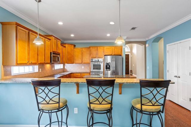 kitchen featuring stainless steel appliances, light stone countertops, hanging light fixtures, and a kitchen bar