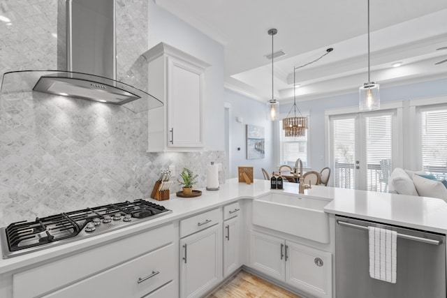 kitchen with pendant lighting, white cabinetry, sink, stainless steel appliances, and wall chimney range hood