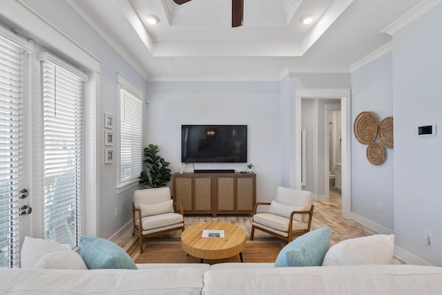 living room featuring ceiling fan, ornamental molding, a tray ceiling, and light hardwood / wood-style floors