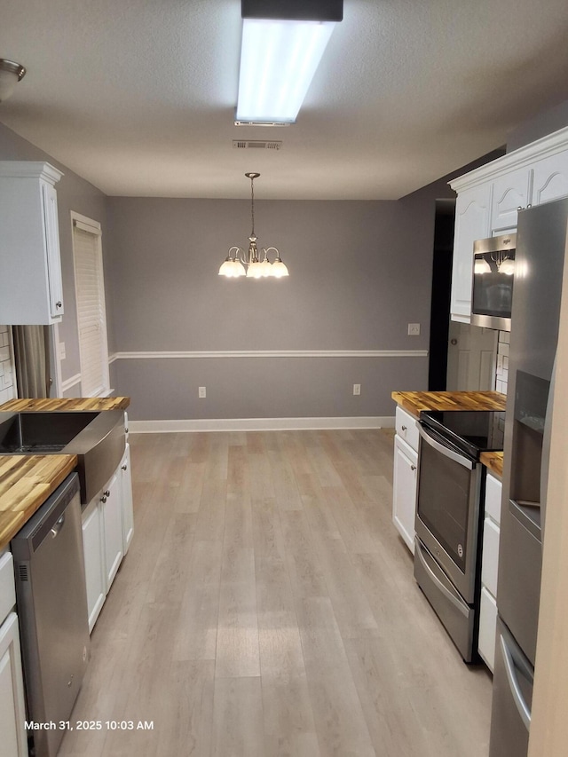 kitchen with wooden counters, white cabinetry, an inviting chandelier, and appliances with stainless steel finishes