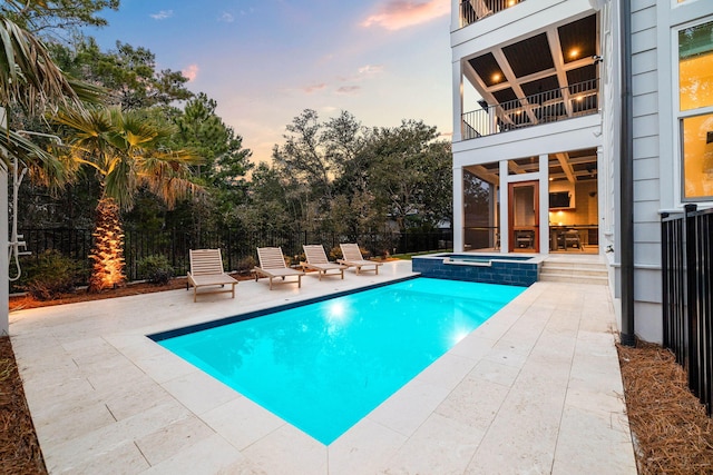 pool at dusk with an in ground hot tub and a patio area