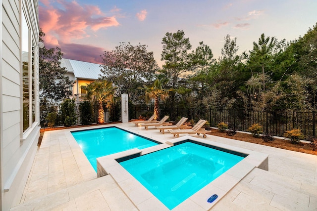 pool at dusk with an in ground hot tub and a patio