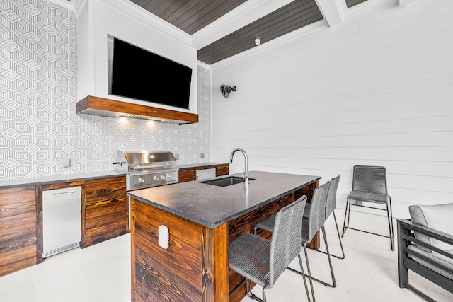 kitchen featuring sink, backsplash, fridge, ornamental molding, and a center island with sink