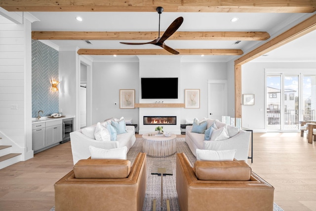 living room with beam ceiling, ornamental molding, light wood-type flooring, beverage cooler, and indoor bar