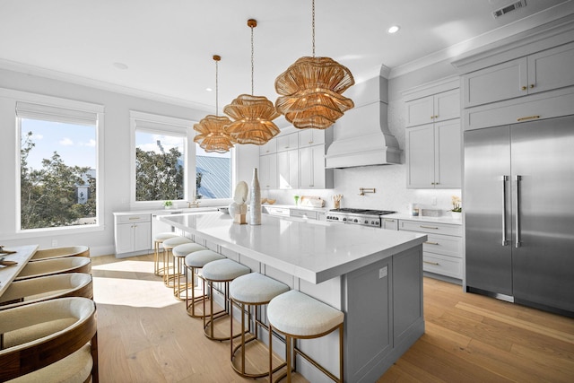 kitchen with built in refrigerator, hanging light fixtures, ornamental molding, a kitchen island, and custom exhaust hood