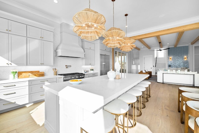 kitchen with pendant lighting, a center island, stainless steel range, custom range hood, and light hardwood / wood-style flooring