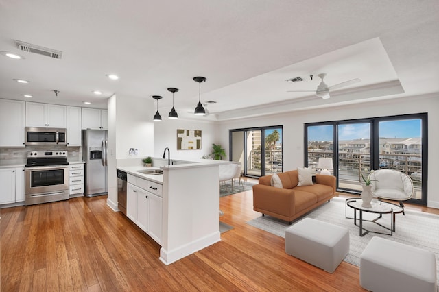 kitchen with appliances with stainless steel finishes, pendant lighting, sink, white cabinets, and a raised ceiling