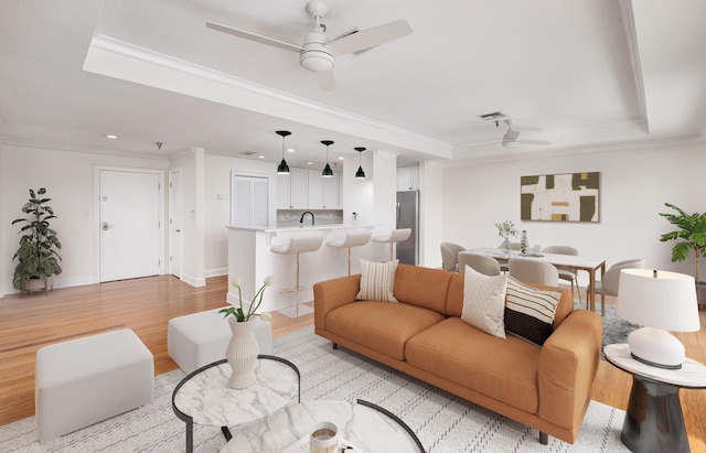 living room featuring sink, crown molding, light hardwood / wood-style flooring, ceiling fan, and a raised ceiling