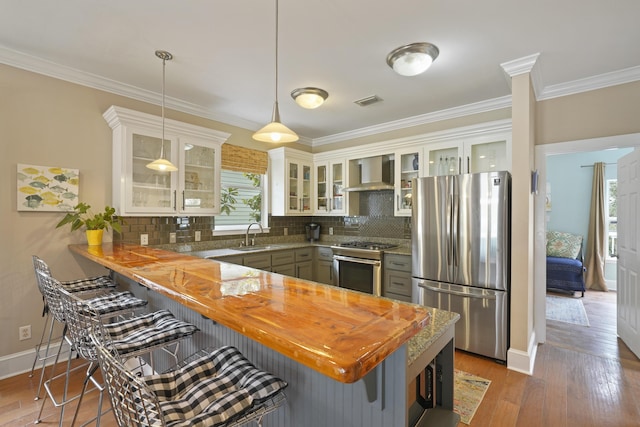 kitchen featuring gray cabinets, hanging light fixtures, stainless steel appliances, kitchen peninsula, and wall chimney exhaust hood