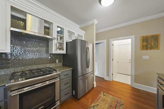 kitchen with white cabinetry, stainless steel appliances, dark stone counters, and wall chimney range hood