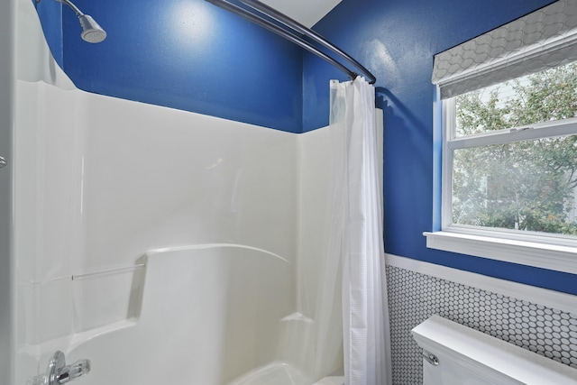 bathroom with a healthy amount of sunlight, shower / bathtub combination with curtain, and toilet