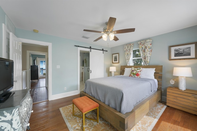 bedroom with ensuite bathroom, a barn door, hardwood / wood-style floors, and multiple windows