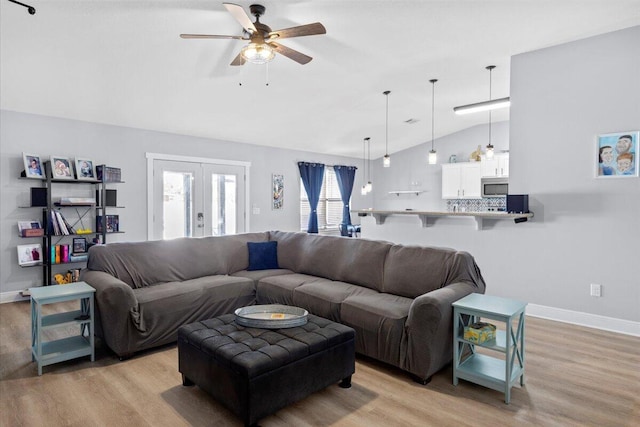 living area with light wood-style flooring, a ceiling fan, baseboards, vaulted ceiling, and french doors