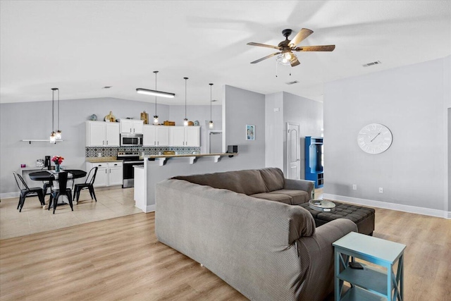 living area with vaulted ceiling, visible vents, a ceiling fan, and light wood-style floors