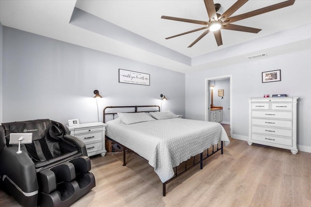 bedroom with light wood-style floors, baseboards, visible vents, and a raised ceiling