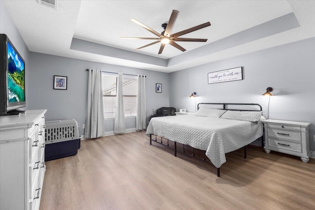 bedroom featuring light wood-type flooring, a tray ceiling, visible vents, and baseboards