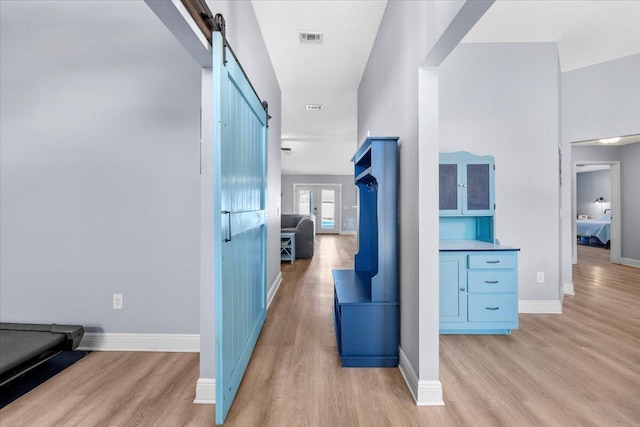 hallway with a barn door, visible vents, light wood-style flooring, and baseboards