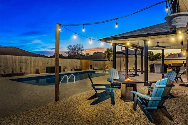 pool at dusk with a fenced in pool, a patio area, ceiling fan, a fenced backyard, and a fire pit