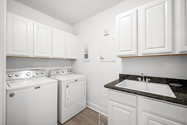 washroom with cabinet space, baseboards, light wood-style flooring, washing machine and clothes dryer, and a sink