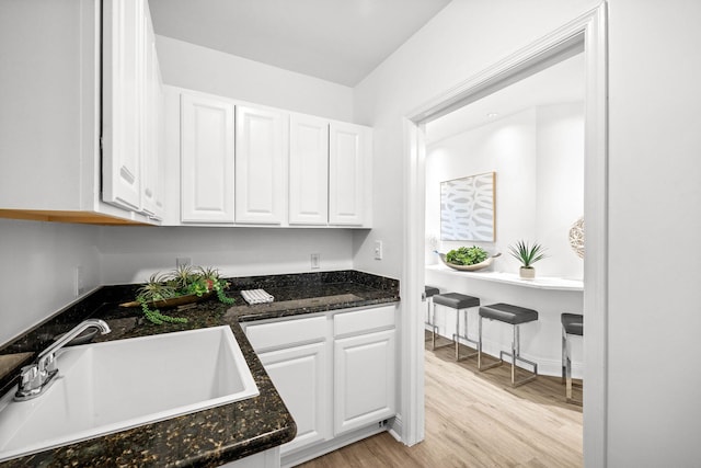 kitchen featuring light wood-style floors, dark stone counters, white cabinets, and a sink