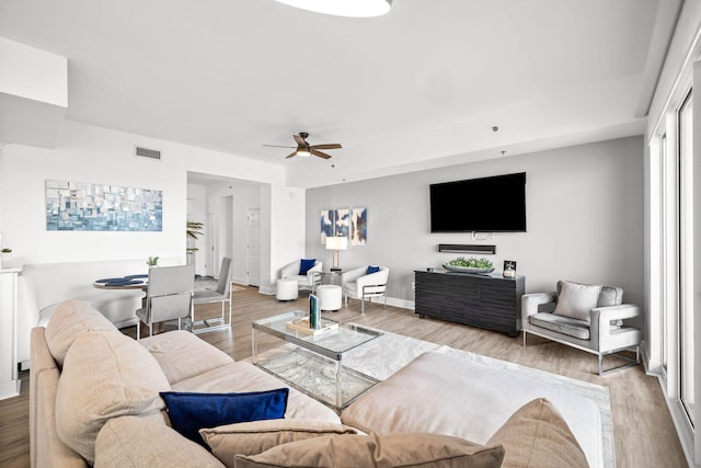 living area featuring a ceiling fan, visible vents, baseboards, and wood finished floors