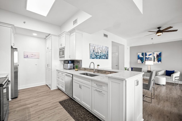 kitchen featuring a peninsula, a sink, white cabinetry, open floor plan, and appliances with stainless steel finishes