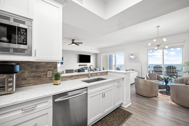 kitchen with decorative backsplash, appliances with stainless steel finishes, open floor plan, a sink, and a peninsula