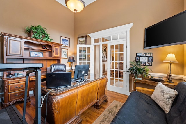 home office featuring a high ceiling, light hardwood / wood-style floors, and french doors