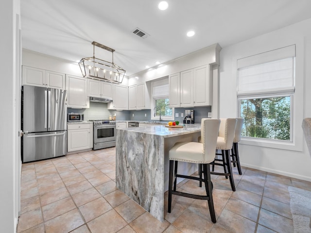 kitchen with pendant lighting, white cabinetry, decorative backsplash, light stone counters, and stainless steel appliances