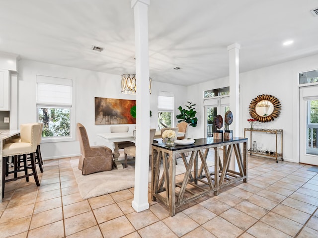 interior space with light tile patterned floors, a wealth of natural light, decorative columns, and a kitchen breakfast bar