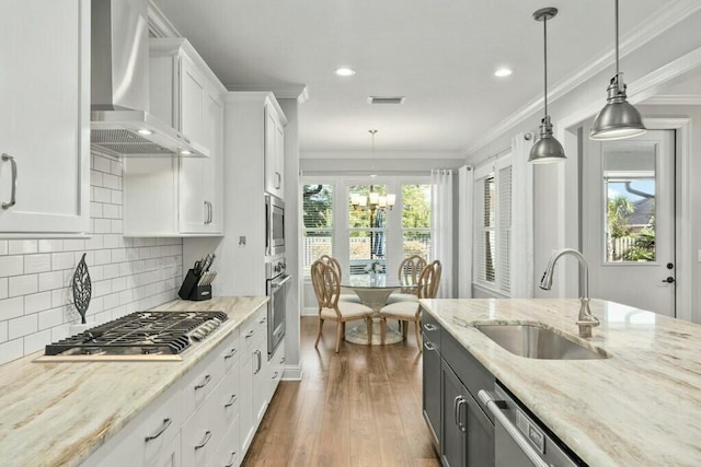 kitchen featuring pendant lighting, white cabinetry, sink, stainless steel appliances, and wall chimney exhaust hood