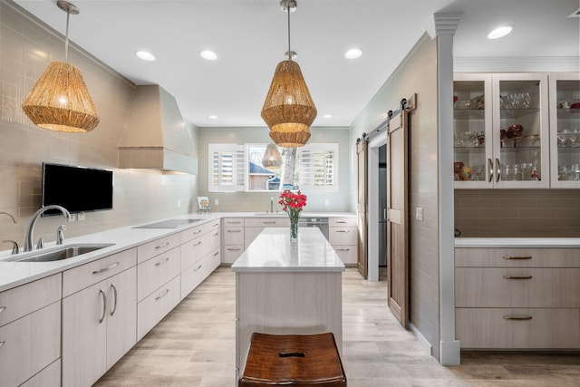 kitchen featuring a barn door, custom range hood, decorative light fixtures, light countertops, and a sink