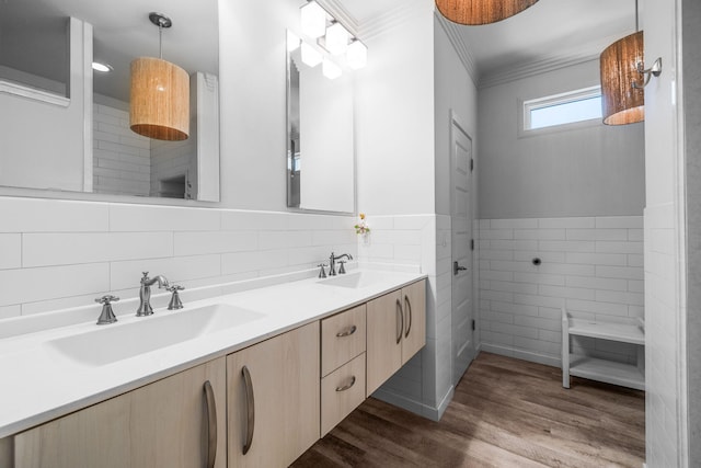 bathroom with double vanity, wood finished floors, a sink, crown molding, and tile walls