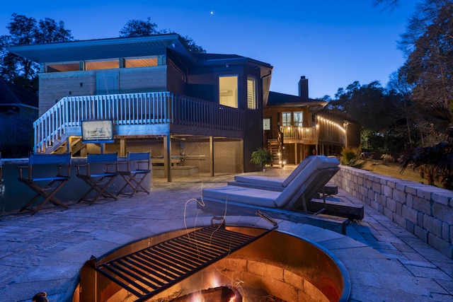 back of property at dusk with stairway, a chimney, a patio area, and a fire pit