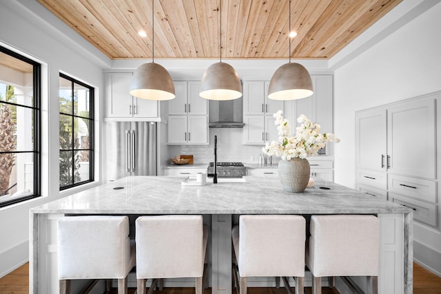 kitchen featuring a large island with sink, light stone countertops, wood ceiling, and decorative light fixtures