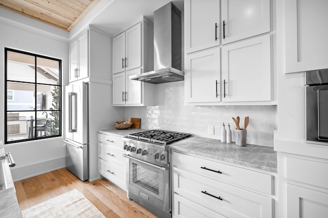 kitchen with wall chimney exhaust hood, tasteful backsplash, light stone counters, stainless steel appliances, and white cabinets