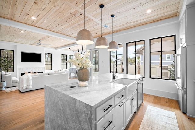 kitchen featuring pendant lighting, wood ceiling, appliances with stainless steel finishes, a kitchen island with sink, and light stone countertops