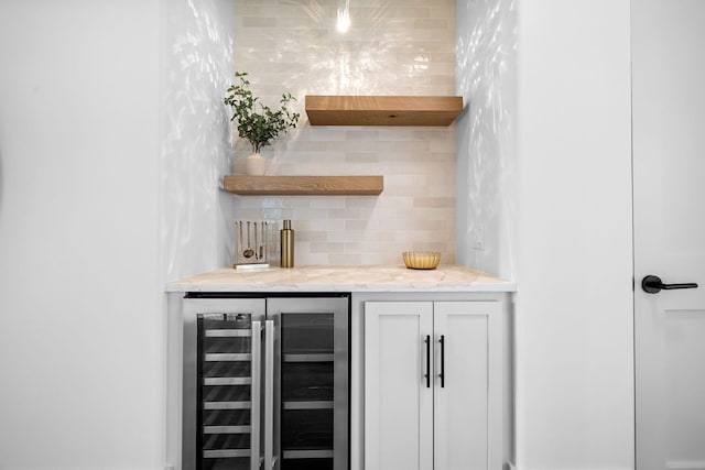 bar with light stone countertops, backsplash, white cabinets, and beverage cooler