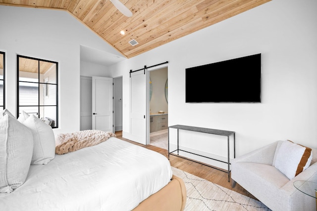 bedroom featuring vaulted ceiling, ensuite bathroom, a barn door, wooden ceiling, and light hardwood / wood-style flooring