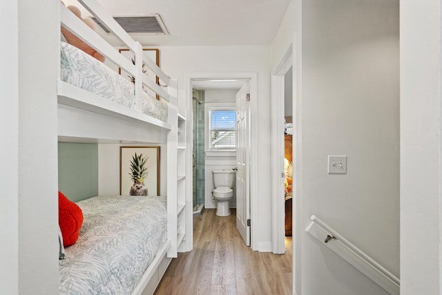 bedroom with light wood-style floors, visible vents, and connected bathroom