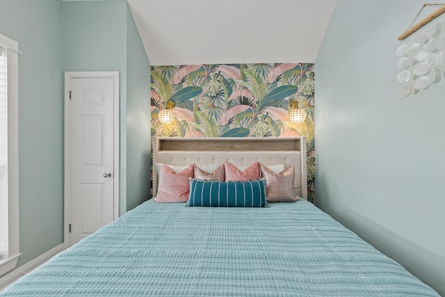 bedroom with lofted ceiling, wallpapered walls, and an accent wall