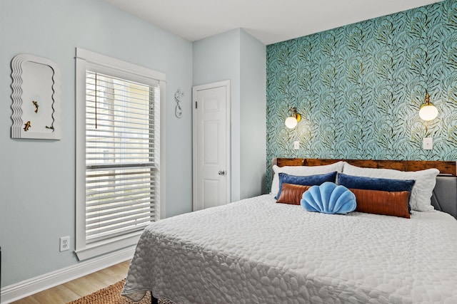 bedroom featuring wallpapered walls, multiple windows, an accent wall, and wood finished floors